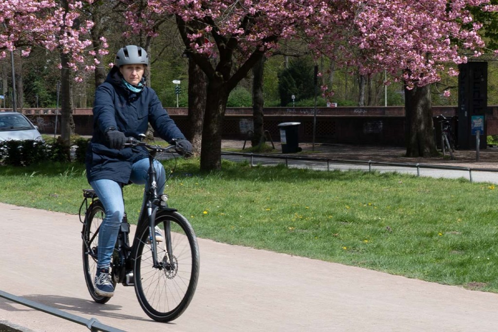 Frau fährt mit City-E-Bike durch Park