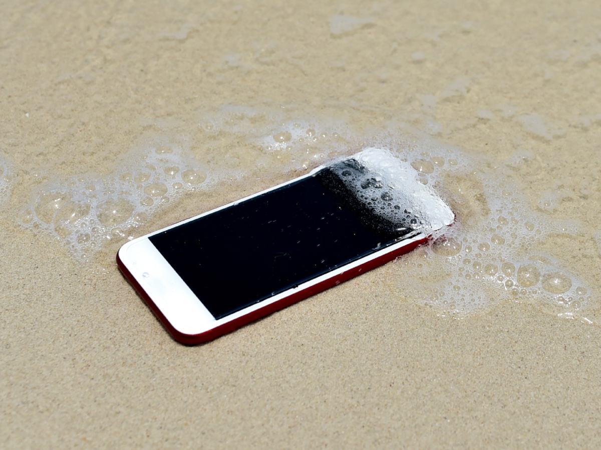 Smartphone liegt am Strand und wird von Meerwasser überspült.