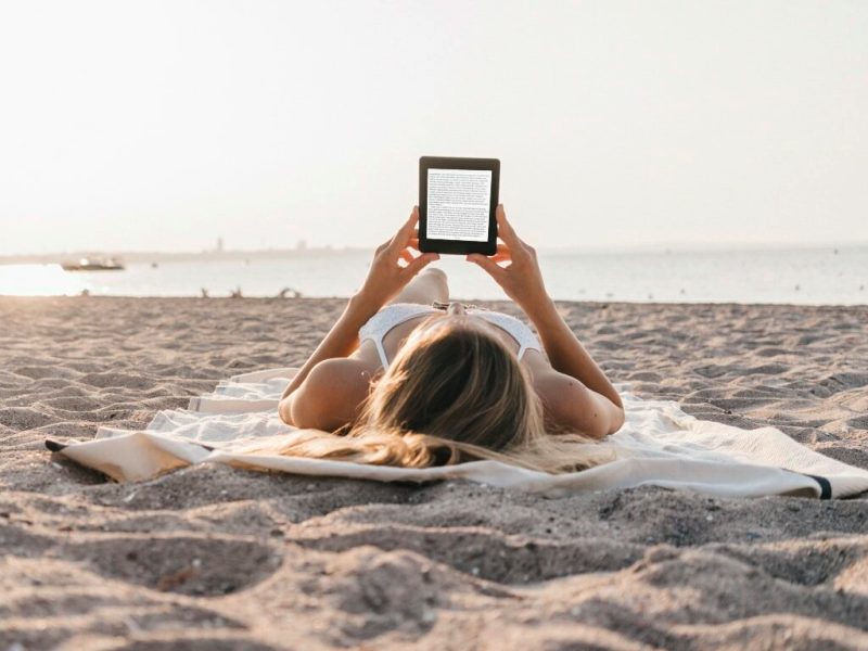 Frau liegt am Strand und liest auf einem EBook-Reader