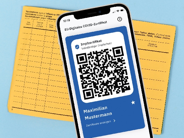 Smartphone mit geöffnetem QR-Code aus CovPass-App liegt auf einem gelben Impfpass.