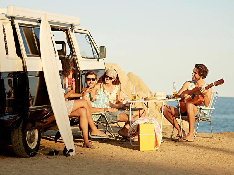 Menschen sitzen am Strand neben VW-Bus