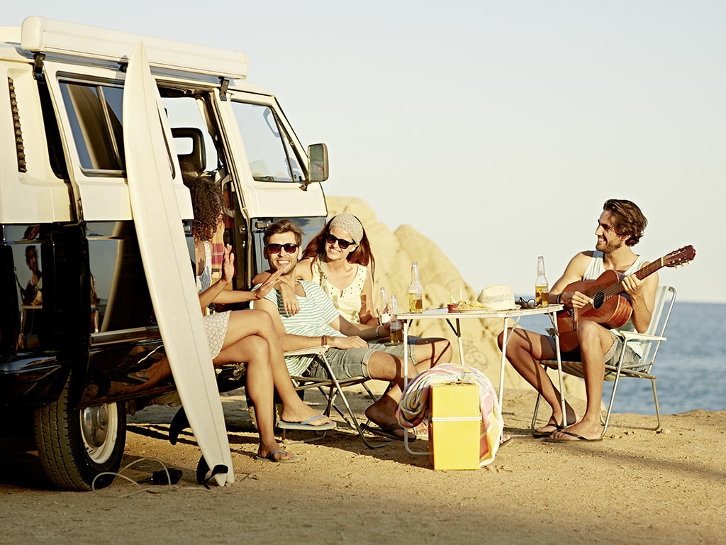 Menschen sitzen am Strand neben VW-Bus