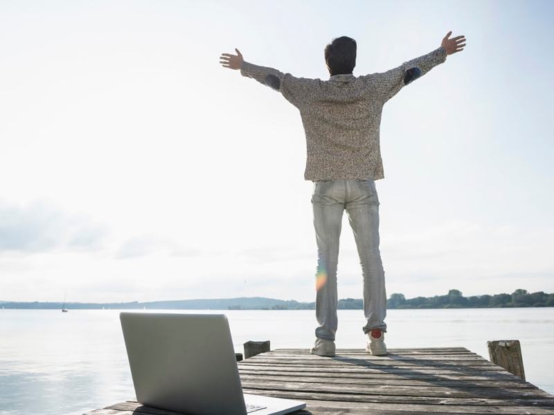 Mann mit Notebook auf Steg am See