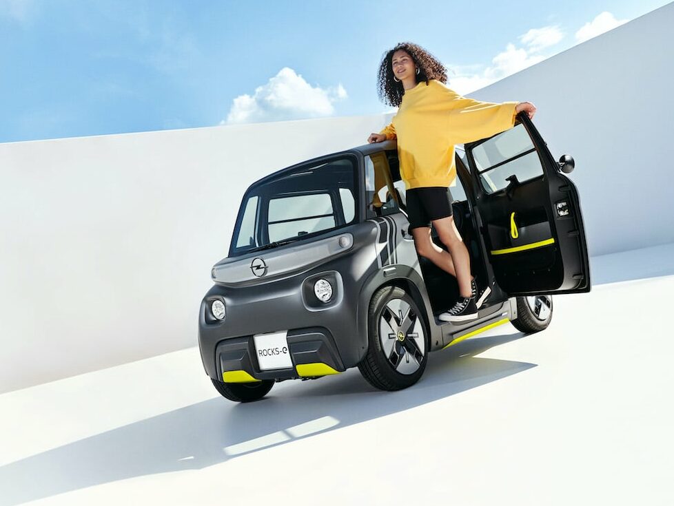 Eine Frau steht vor einem Kleinwagen mit Elektroantrieb.