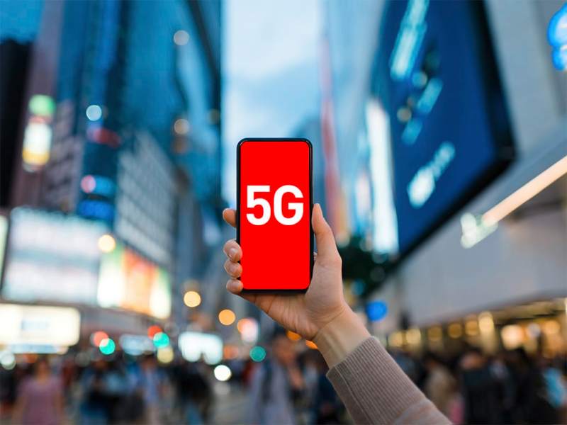 Woman's hand using smartphone against illuminated financial district in the city, with the concept of 5G communications technology