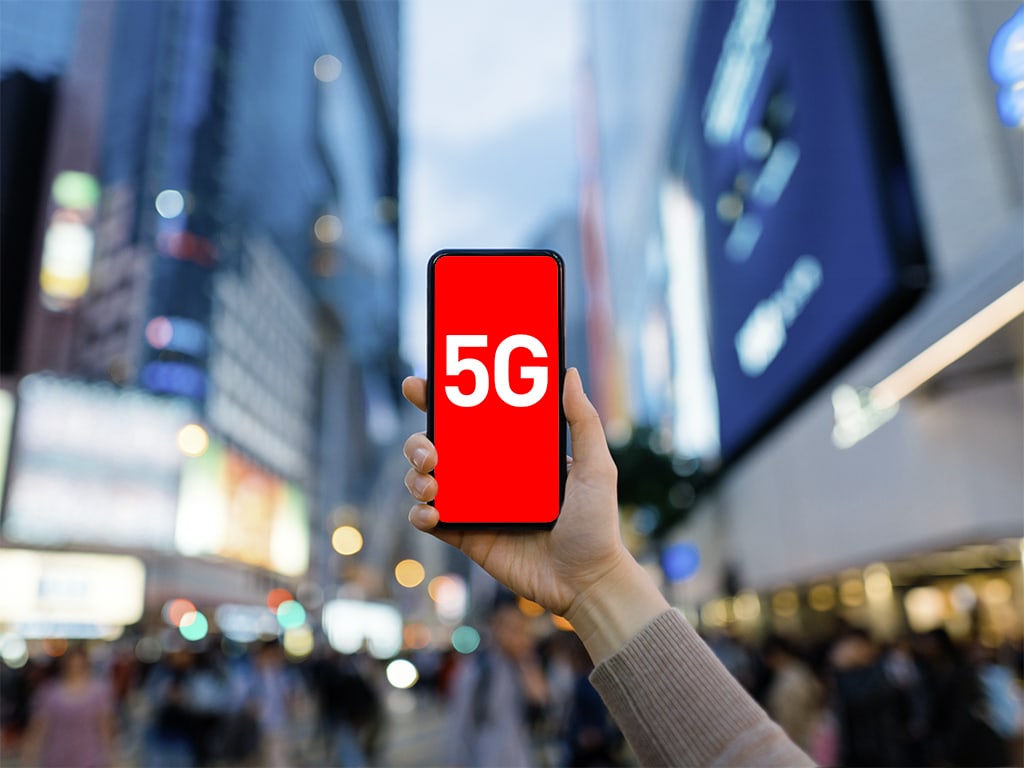 Woman's hand using smartphone against illuminated financial district in the city, with the concept of 5G communications technology