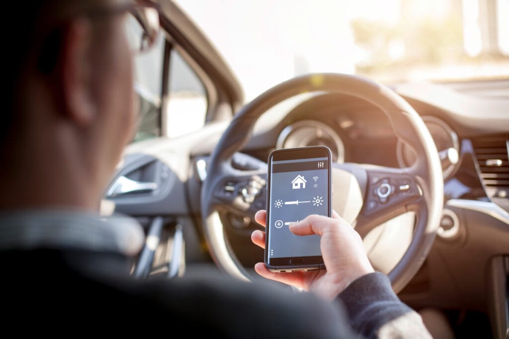 Blick über die Schulter eines Mannes, der im Auto sitzt und sein Smartphone bedient