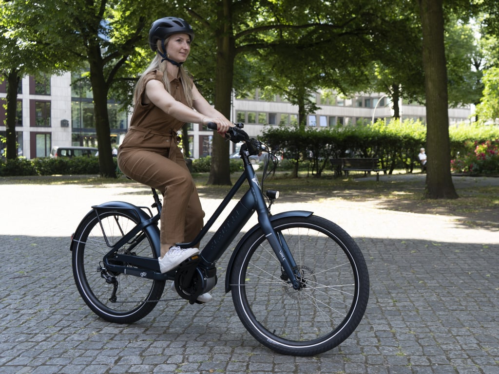 Frau auf dunklem E-Bike fährt auf Pflasterweg