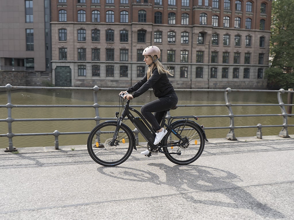 Frau fährt auf E-Bike auf Weg am Fluss in der Stadt