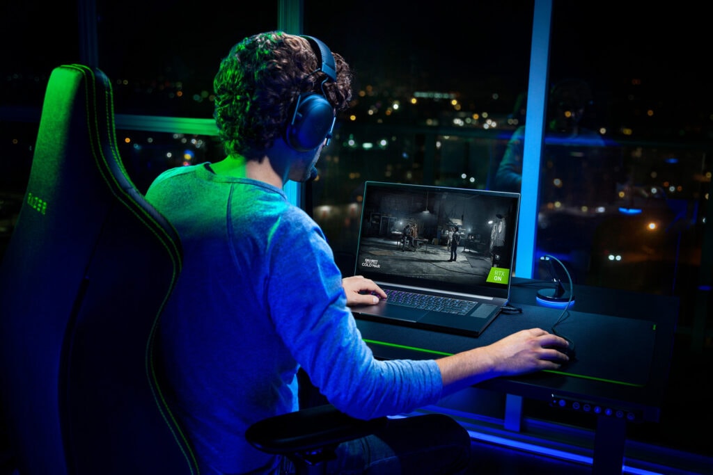 Junger Mann auf Bürostuhl mit Headset benutzt das Razer am Schreibtisch bei dunklem Licht