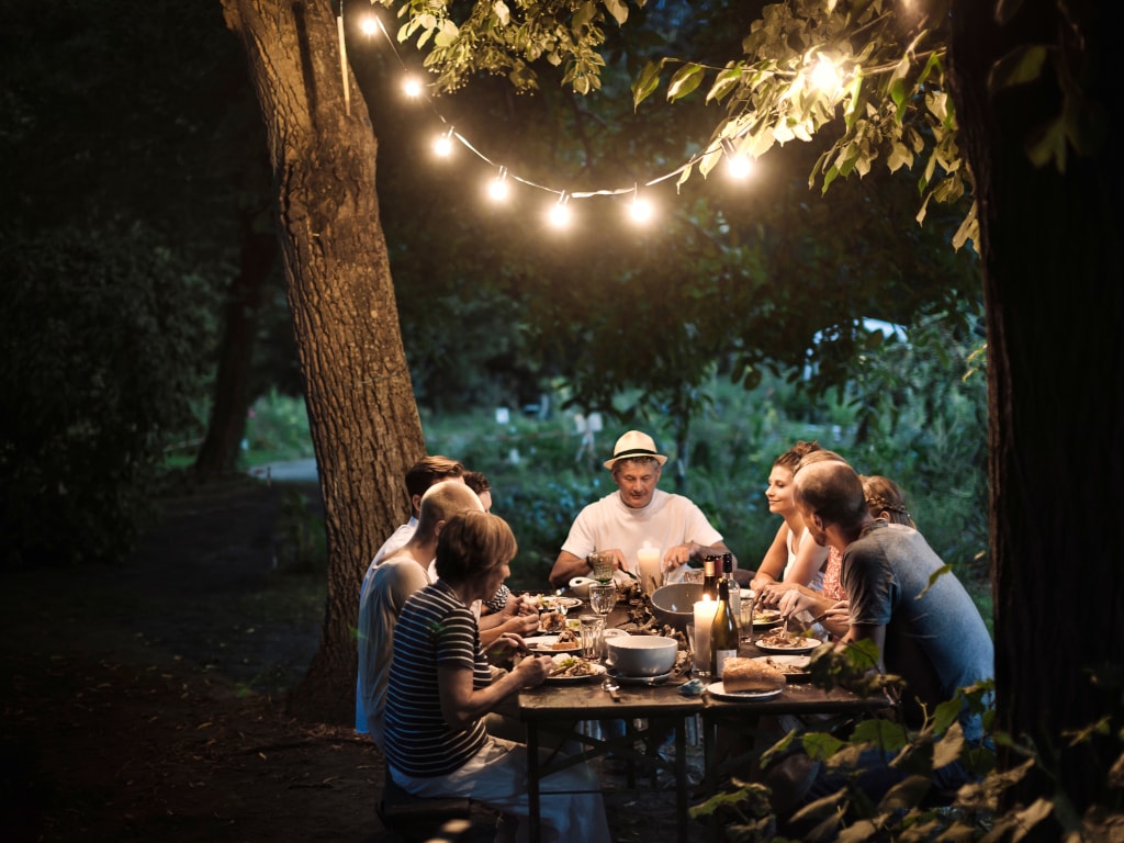 Freunde am gedeckten Tisch im Garten bei Dunkelheit beleuchtet von Lichterkette