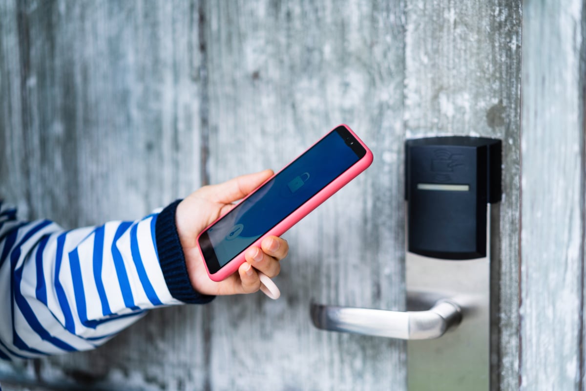 Hand hält Smartphone an smartes Türschloss an grauer Holztür