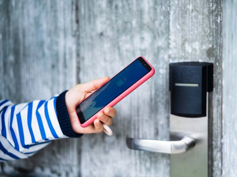 Hand hält Smartphone an smartes Türschloss an grauer Holztür