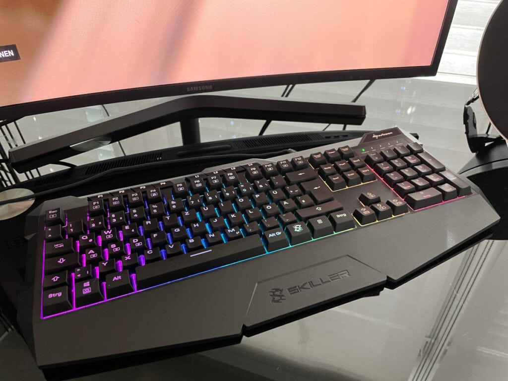 Schwarze Tastatur mit leuchtenden Tasten auf Glastisch vor schwarzem Bildschirm