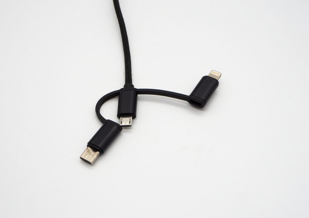 Schwarzes USB-Kabel kommt von oben ins Bild, darunter liegt ein kurzes schwarzes Kabel auf weißem Hintergrund