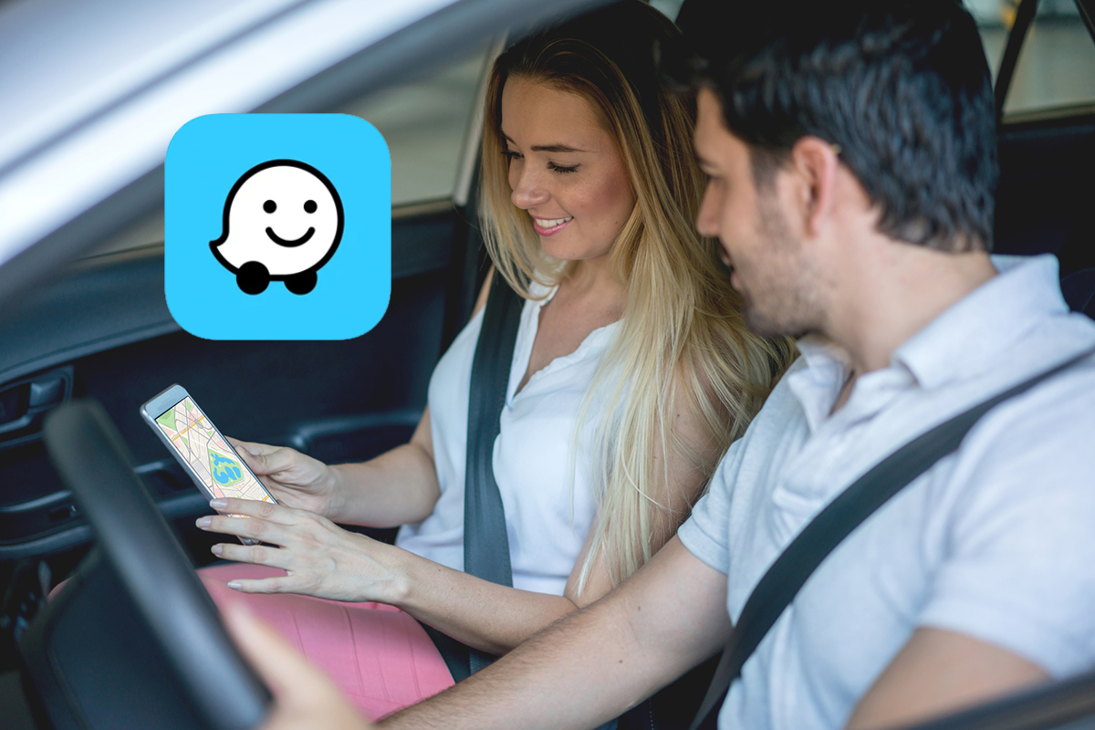 Junges Paar sitzt lächelnd im Auto und schaut auf Smartphone, das die Frau hält