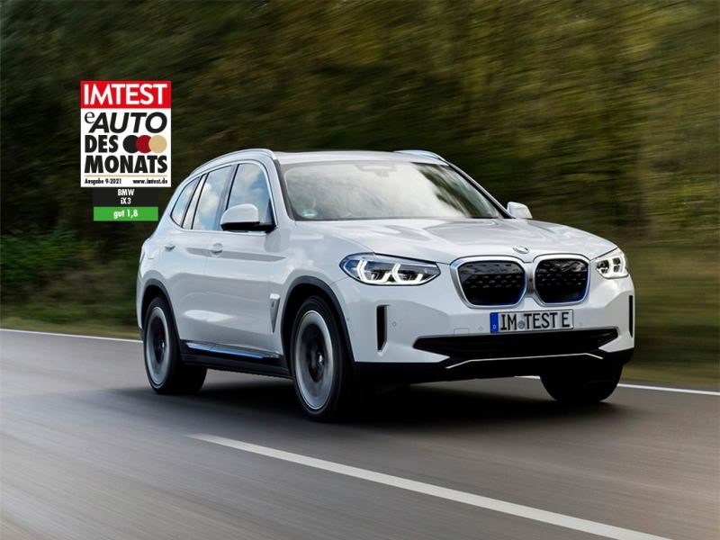 Silberner SUV von BMW fährt auf Straße am Wald mit dem IMTEST-Siegel "E-Auto des Monats"