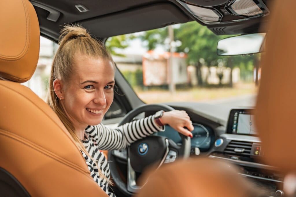 Frau sitzt am Steuer im Auto und schaut lächelnd über die Schulter