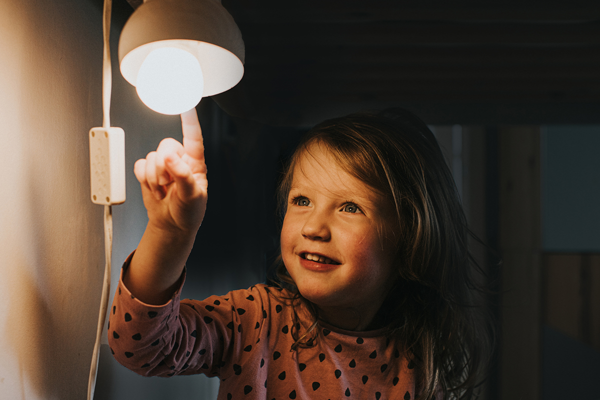 Kleines Mädchen berührt eine Glühbirne mit dem der Fingerspitze.
