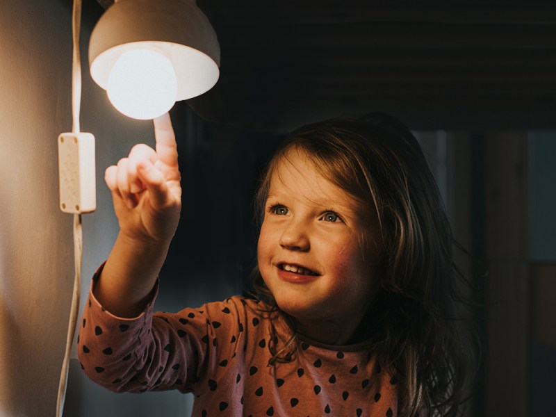Kleines Mädchen berührt eine Glühbirne mit dem der Fingerspitze.
