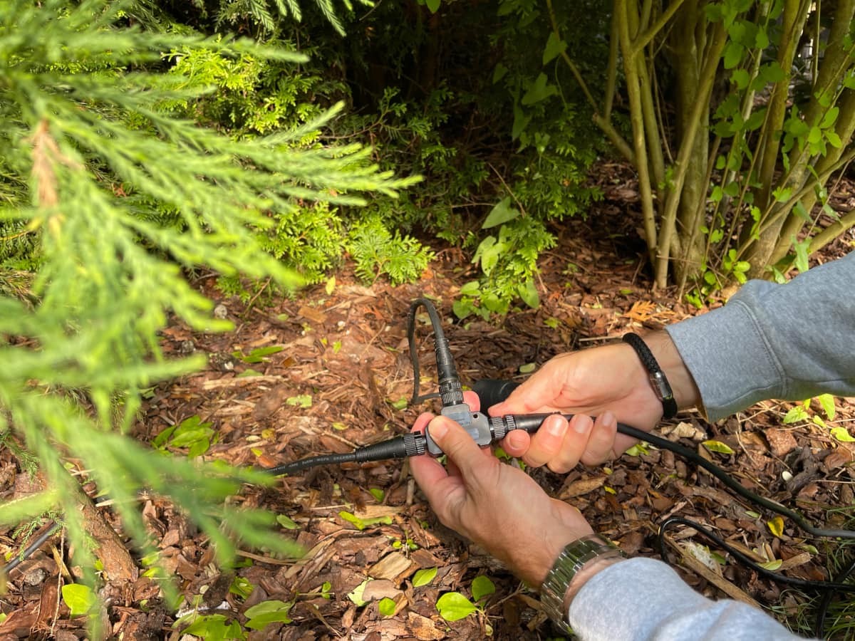 Zwei Hände schrauben Verbindungsstück und Kabel zusammen auf Gartenboden