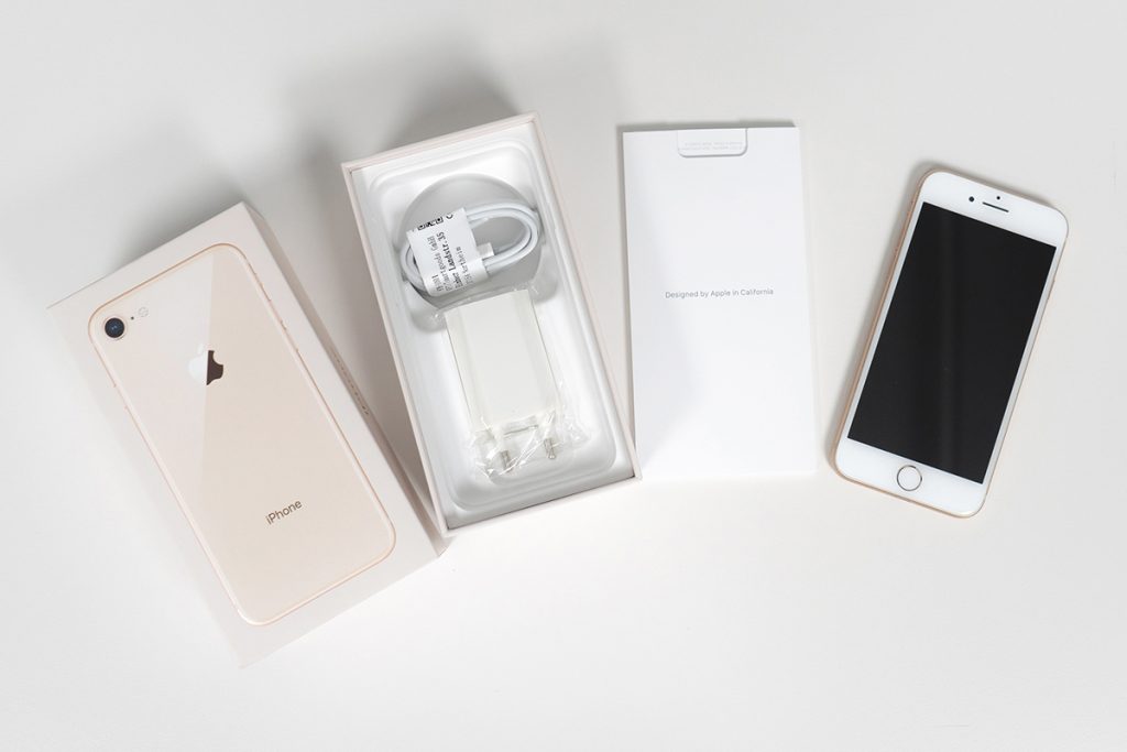 Weißes iPhone in Reihe angeordnet mit Anleitung und Verpackung auf grauem Hintergrund