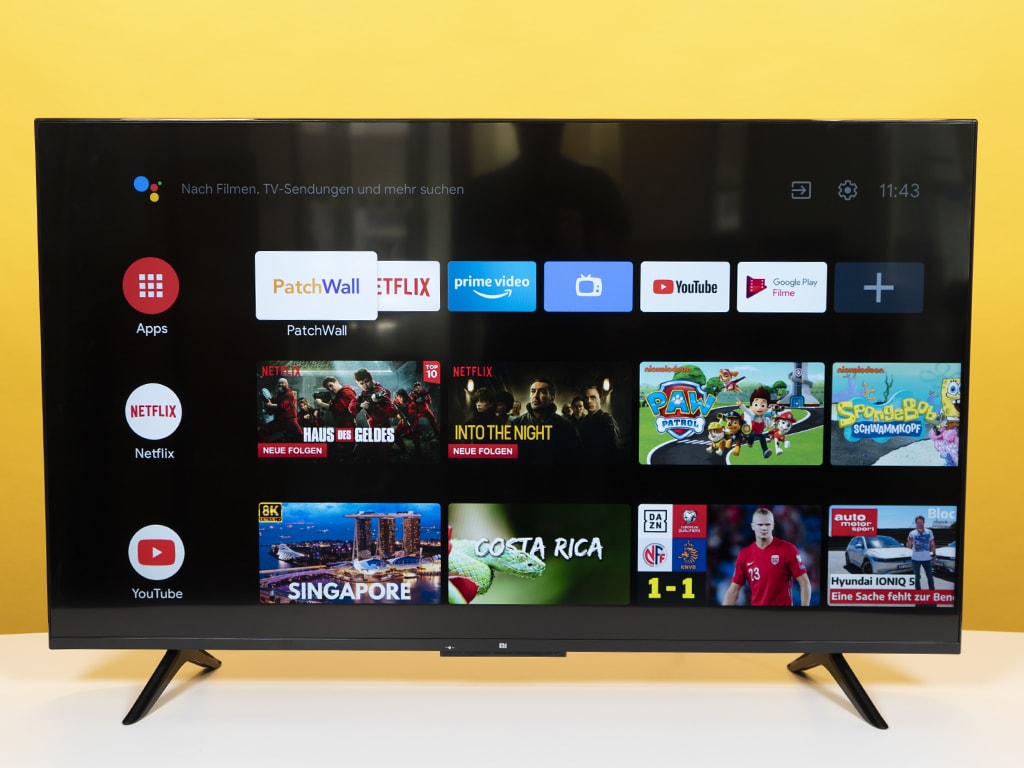 Fernseher zeigt verschiedene Apps auf weißem Tisch mit gelben Hintergrund