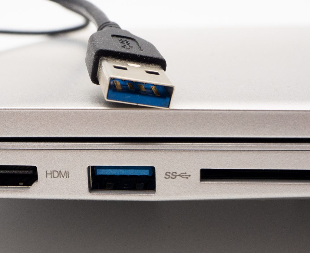 Detail zugeklapptes silbernes Notebook mit USB Ports und USB Stecker mit blauer Farbe