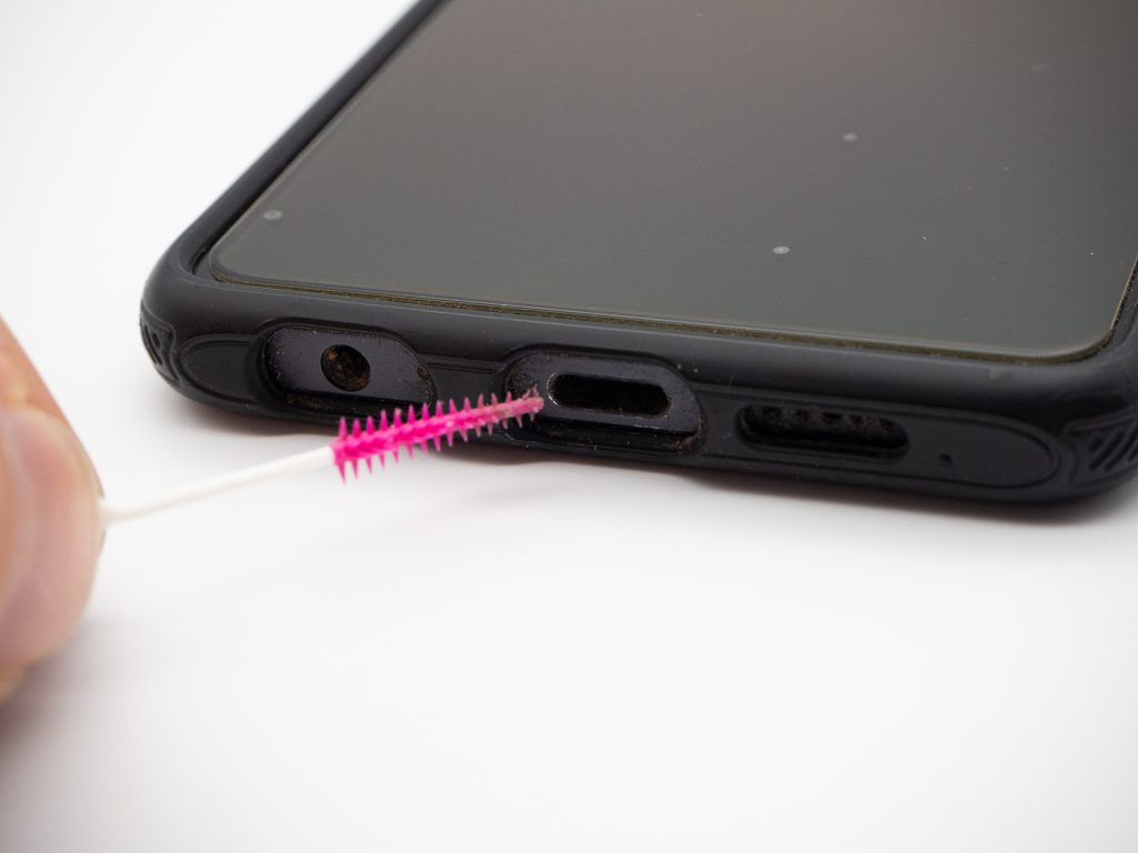 Hand hält pinke Zahnpflegebürste an USB-Schnittstelle von schwarzem Handy auf weißem Hintergrund