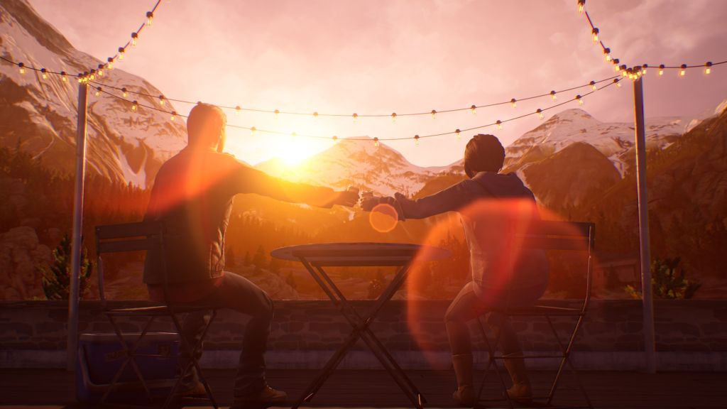 Von hinten: Mann und Frau sitzen draußen vor Bergkulisse auf Holzstühlen und stoßen mit Getränkedosen über den runden Tisch hinweg an