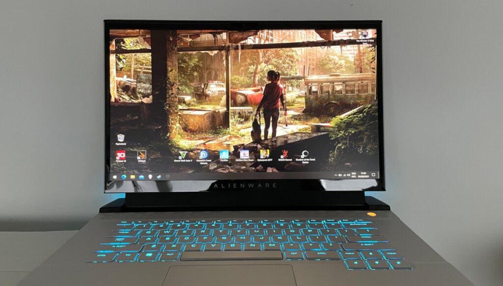 Graues Notebook mit türkis leuchtender Tastatur aufgeklappt von vorne, Bildschirm zeigt Desktop mit Bild aus Spiel
