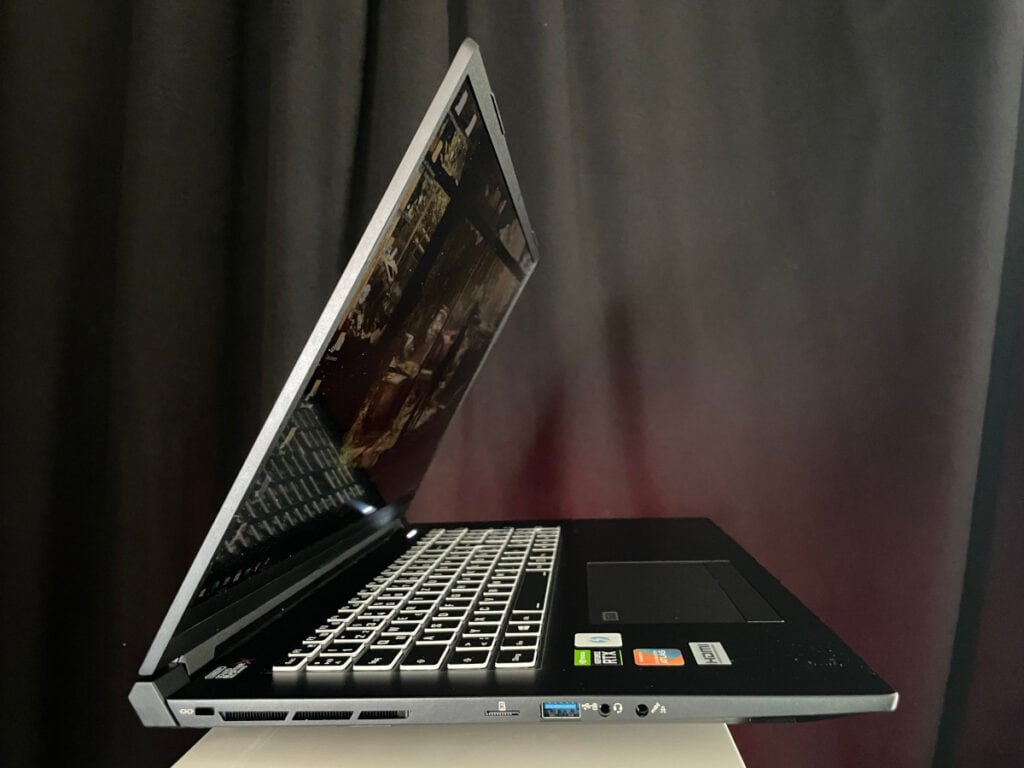 Silberner halb aufgeklappter Laptop auf grauem Podest vor dunklem Vorhang