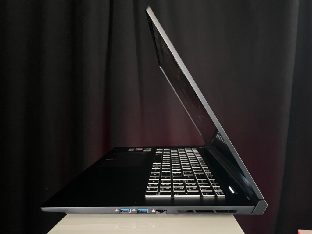 Silberner Laptop halb aufgeklappt von der Seite auf grauem Podest vor dunklem Vorhang
