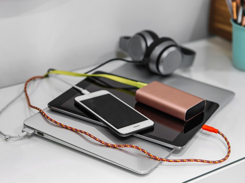 Silbernes zugeklapptes Notebook auf dem weißes Smartphone, braune externe Festplatte und Kopfhörer liegen auf weißem Tisch