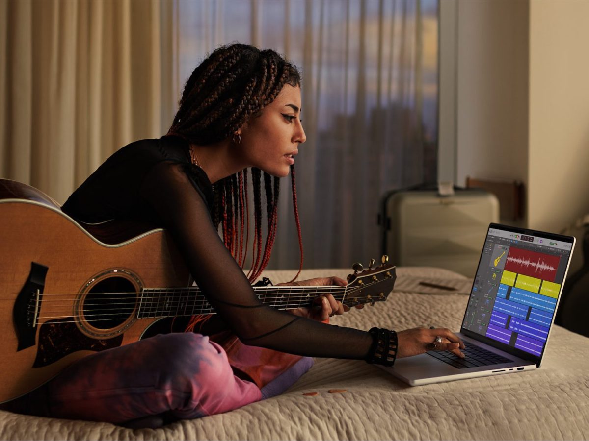 Eine Frau mit eine Gitarre sitzt vor einem MacBook