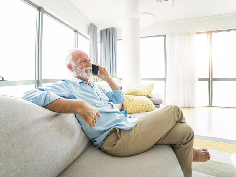 Älterer Mann sitz auf Sofa und telefoniert per Smartphone