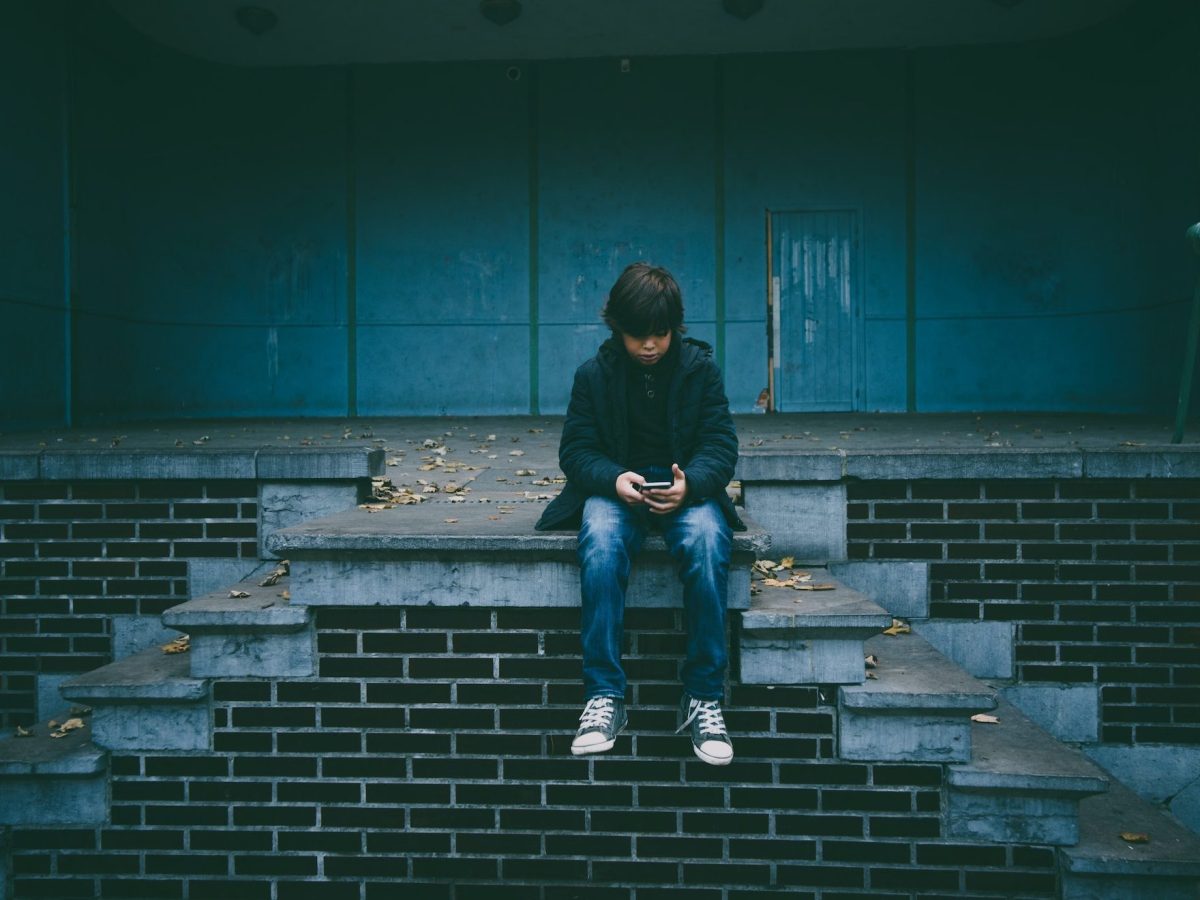 Ein Kind mit Smartphone sitzt auf einer Mauer