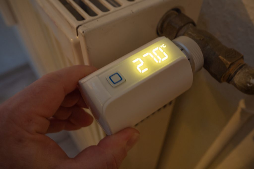 Hand hält leuchtendes Thermostat an Heizung