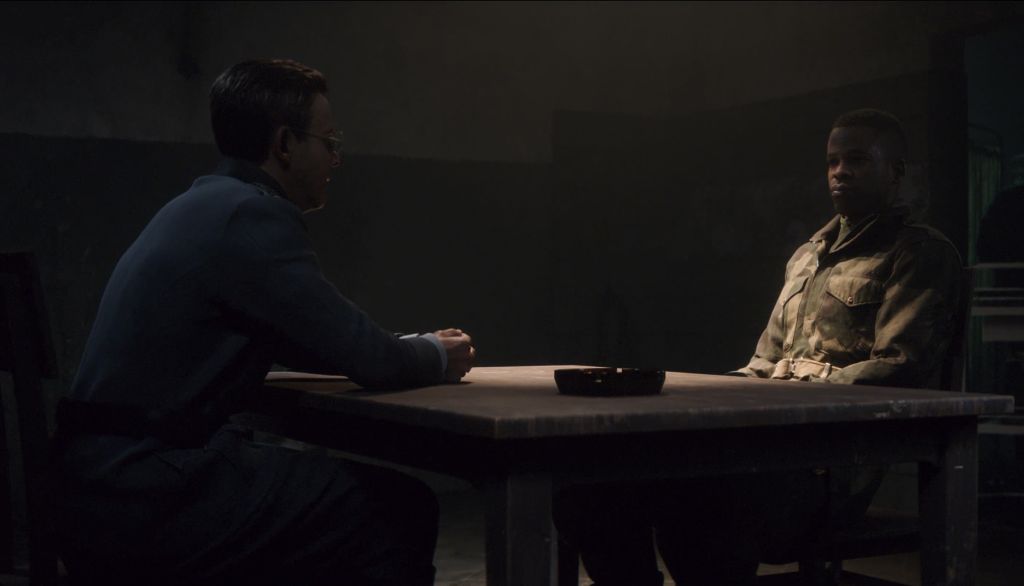 Screenshot Zwei Männer an einem Tisch im dunkeln