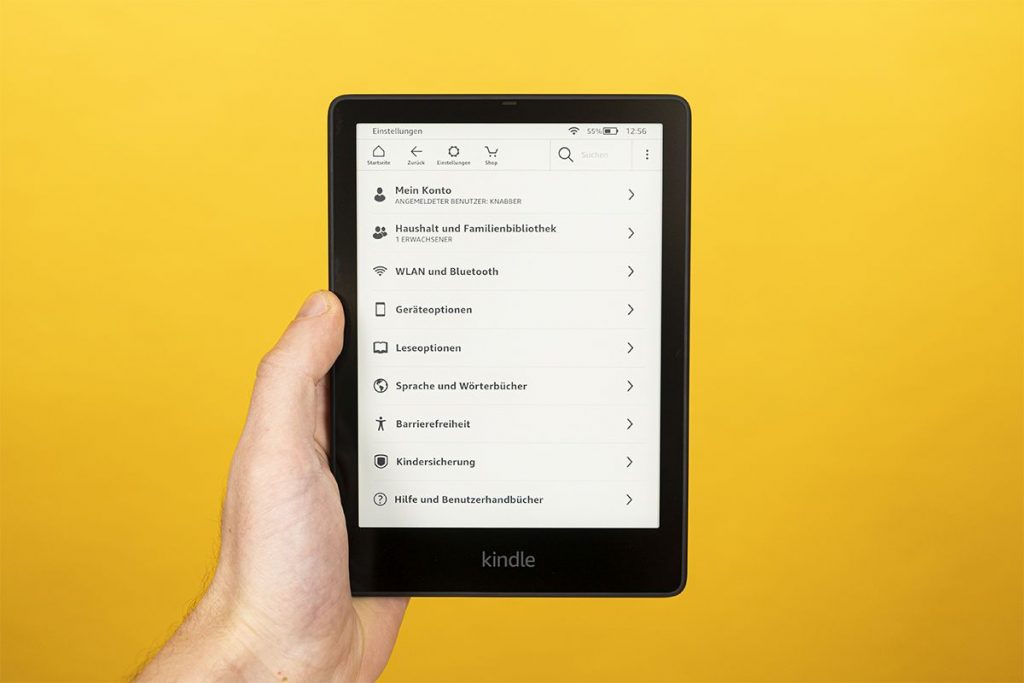 Hand hält Kindle, der Einstellungen anzeigt vor gelber Wand