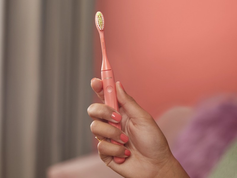 Hand mit Rosa lackierten Fingernägeln hält rosa Zahnbürste
