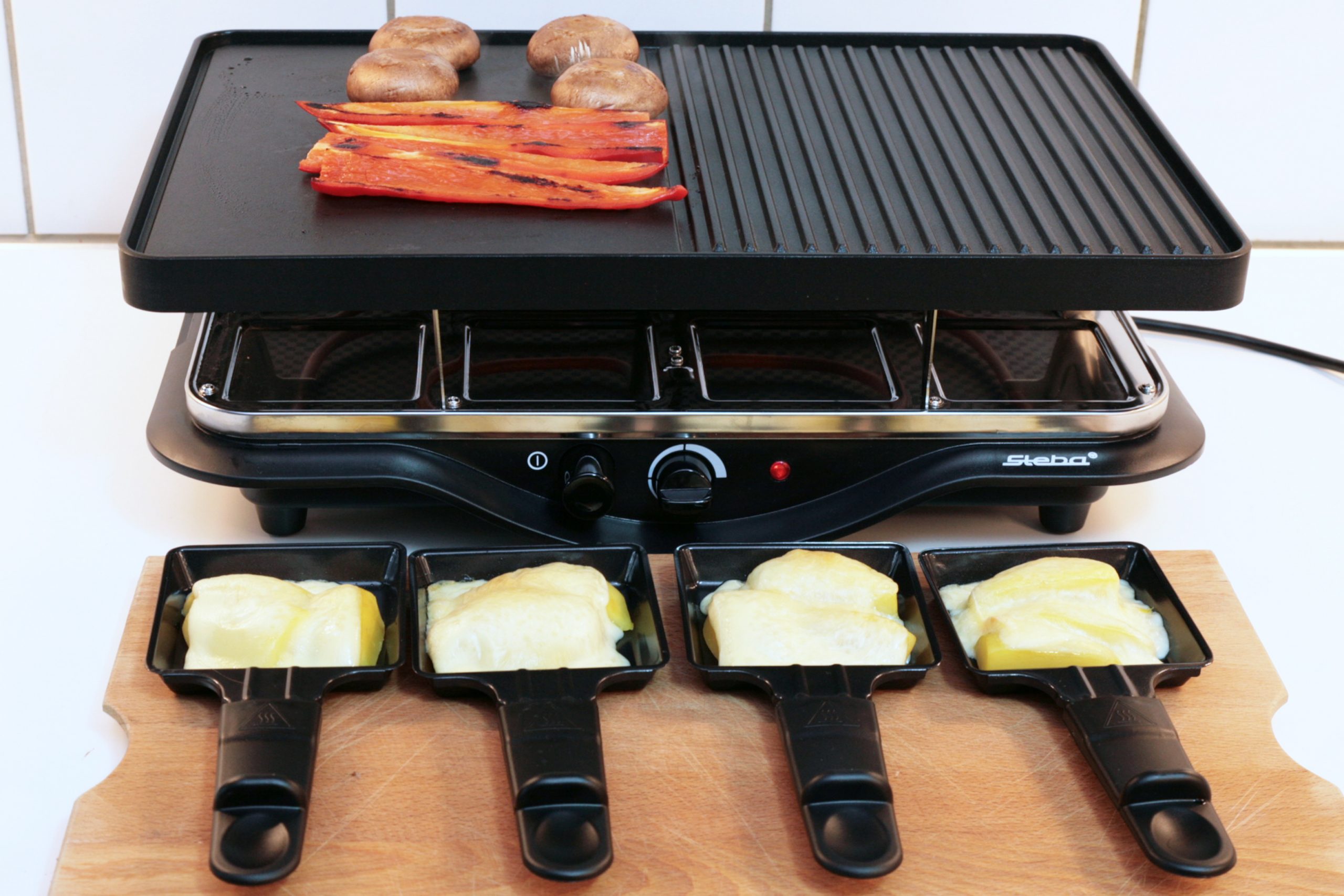 Raclette Pfannen befüllt mit schmelzendem Käse vor Grill