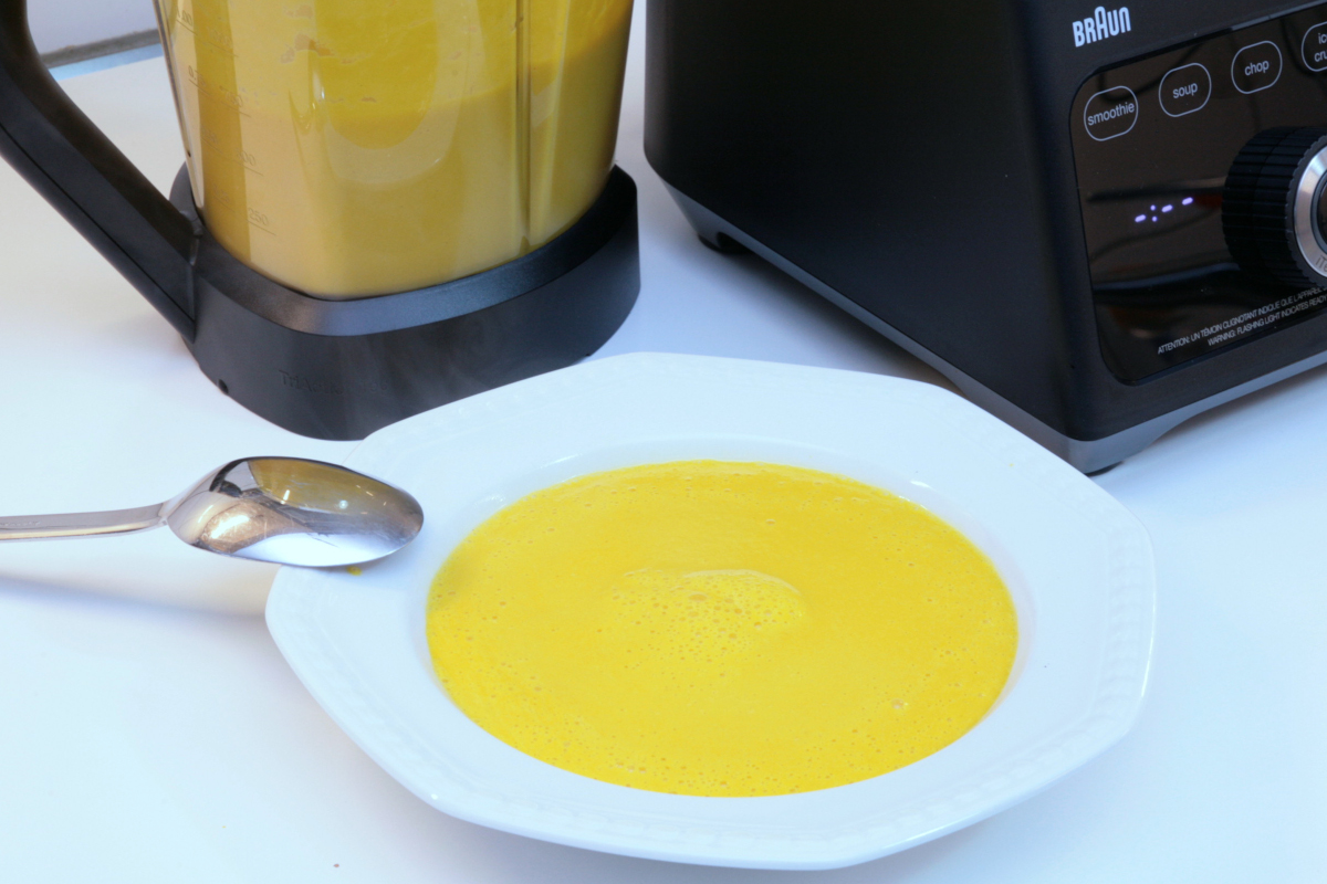 Pürierte gelbe Suppe auf Teller vor Mixer