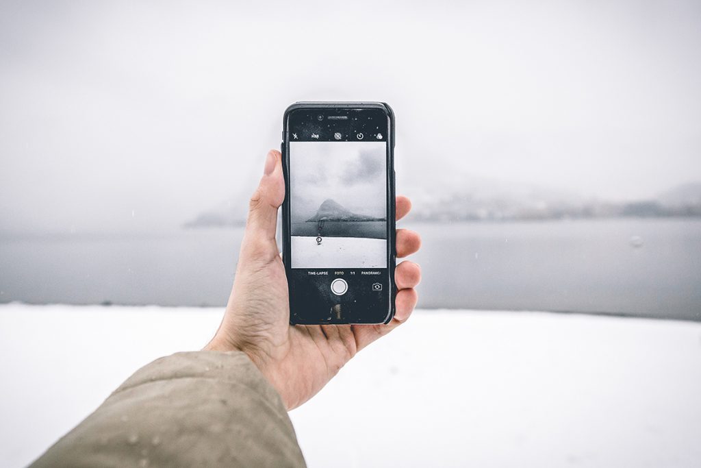 Hand die ein Smartphone hält, und eine Schneelandschaft fotografiert.