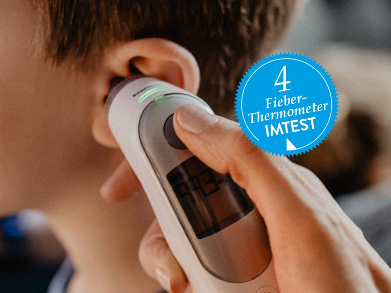 Ein Fieberthermometer wird an das linke Or eines Kindes gehalten.