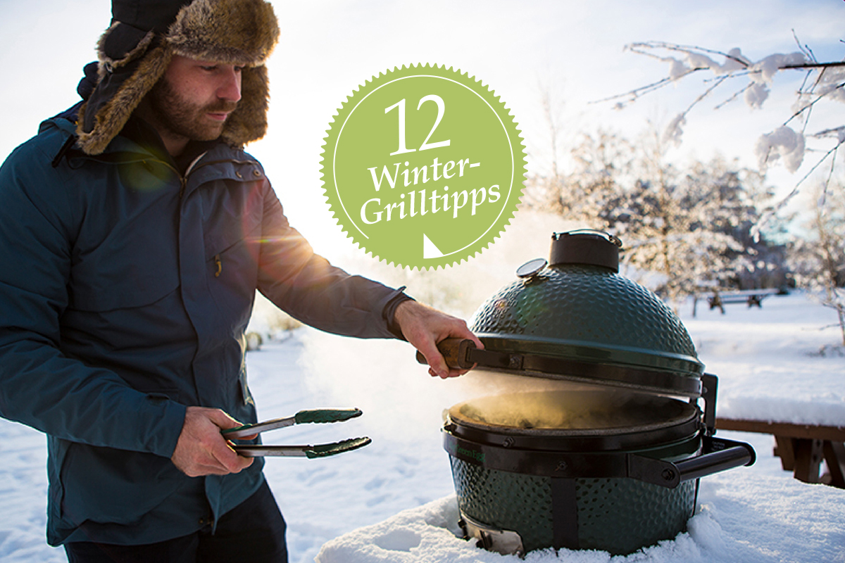 Ein Mann steht im Schnee an einem Grill.