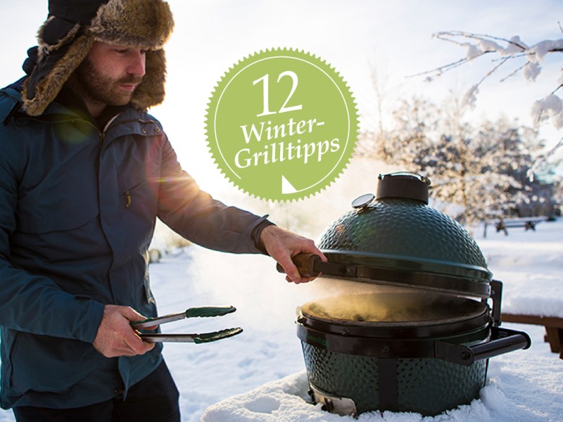 Ein Mann steht im Schnee an einem Grill.