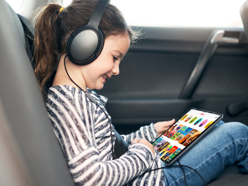 Mädchen sitzt im Auto und guckt Netflix Kids auf Tablet.