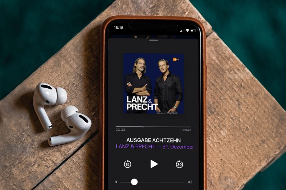 Auf einem iPhone läuft der Lanz und Precht-Podcast, daneben zwei Kopfhörer.