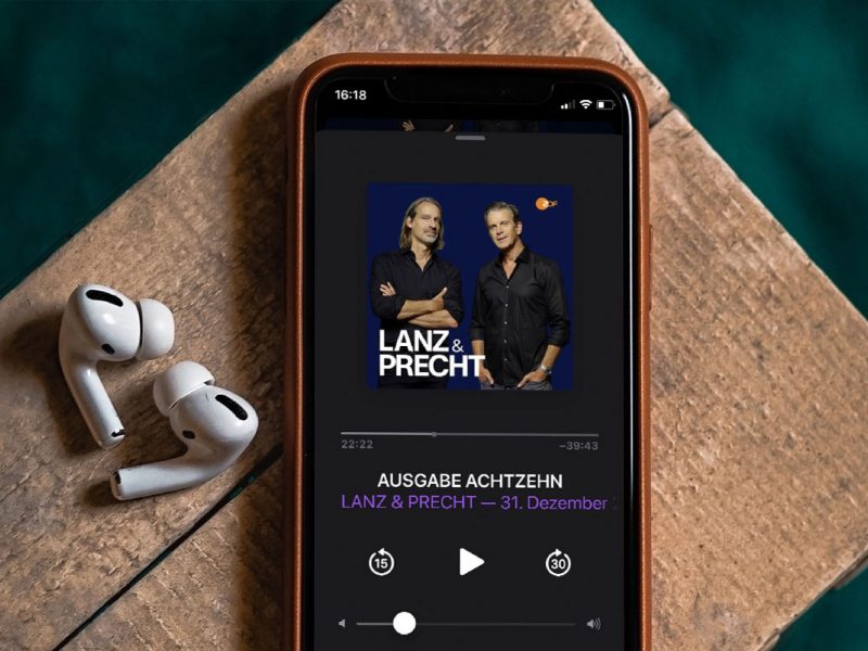 Auf einem iPhone läuft der Lanz und Precht-Podcast, daneben zwei Kopfhörer.